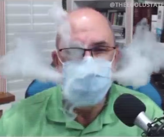 Photo of a doctor in surgical uniform, and wearing a surgical mask, breathing out smoke all around and through the mask.